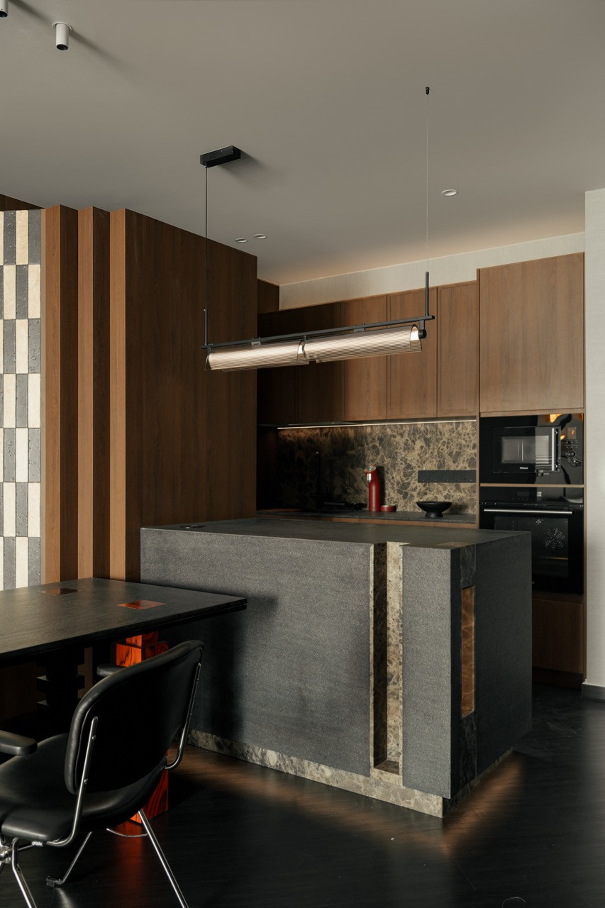 The open-plan living and dining area, with the checker-tiled niche wall, kitchen beyond, and the edge of the black leather sofa at left