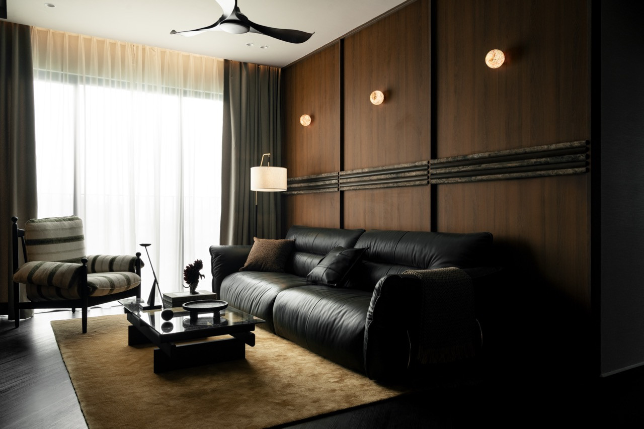 The living room in full, with the black leather sofa, low black coffee table, a striped armchair at the window and two amber globe sconces set into the panelled feature wall