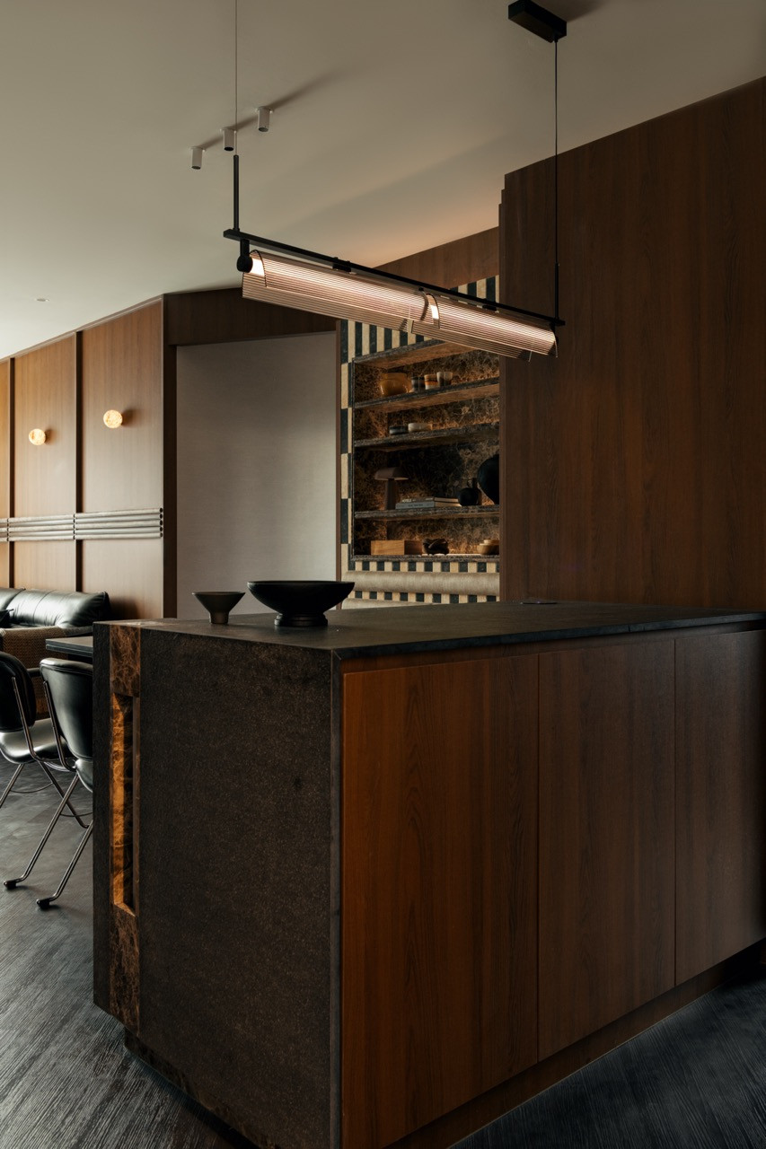A credenza in the living area, with red-orange figured wood shelves mounted on a grey fabric wall holding ceramics, stone spheres and small objects