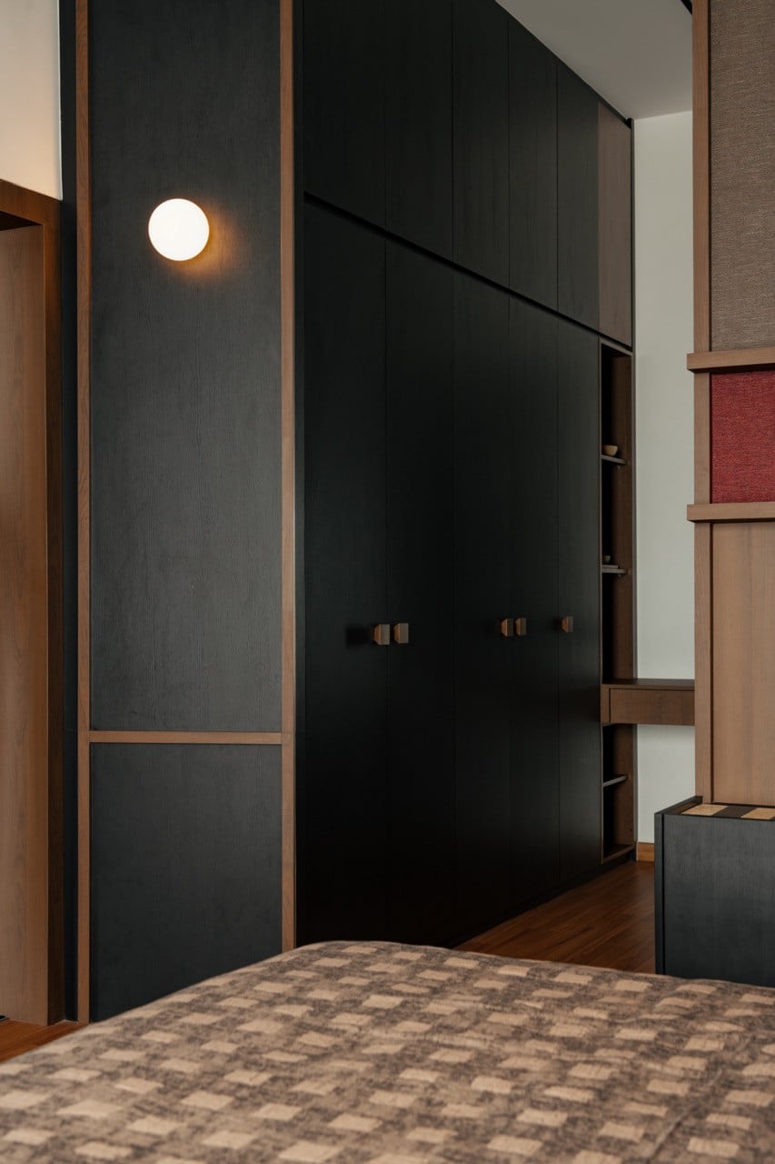 The dark charcoal built-in wardrobe with bronze hardware, set against warm wood-panelled walls, with a globe wall light mounted to the left