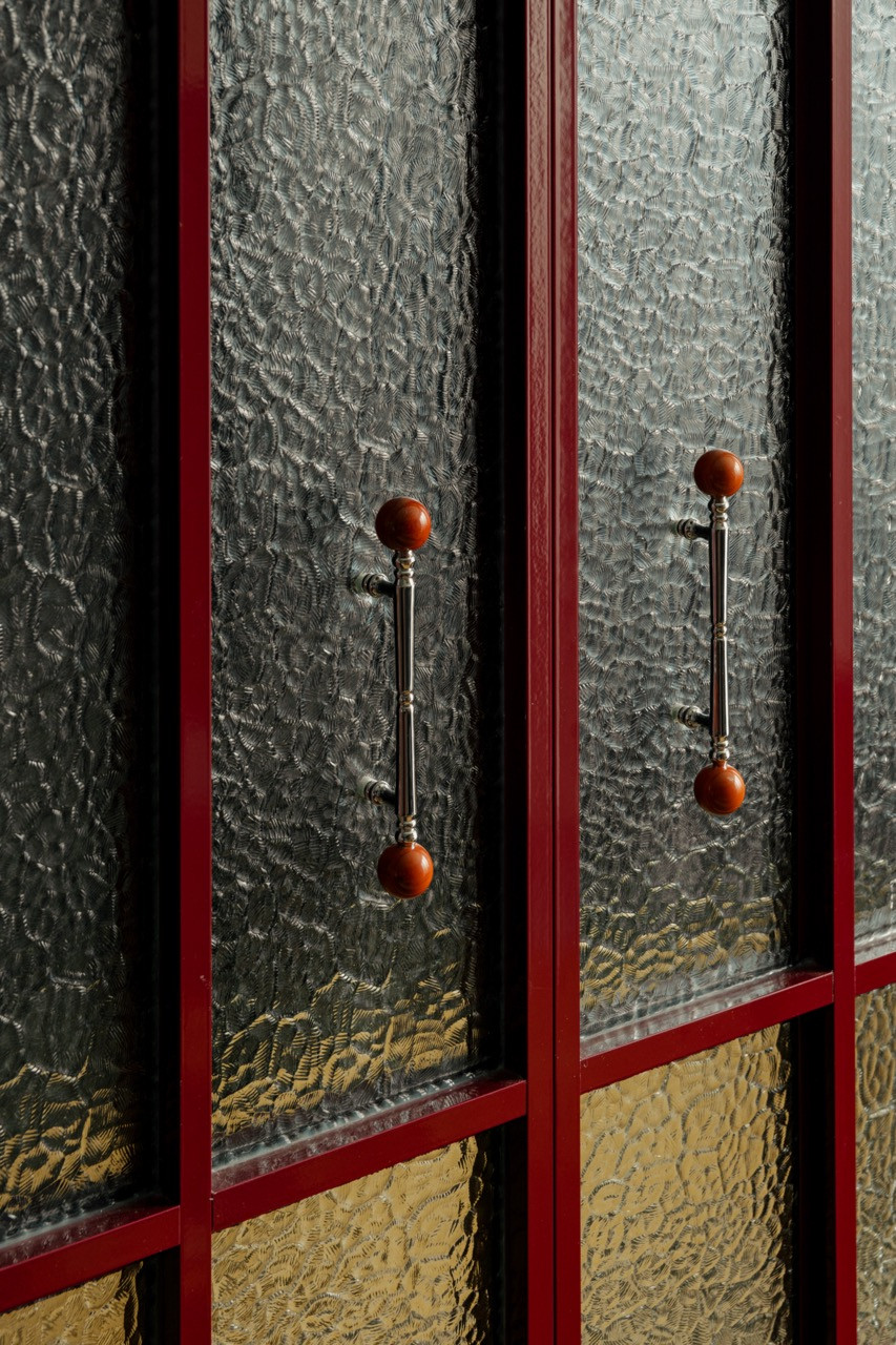 Close detail of the reeded glass cabinet doors in crimson-lacquered frames, with turned wood and chrome pull handles