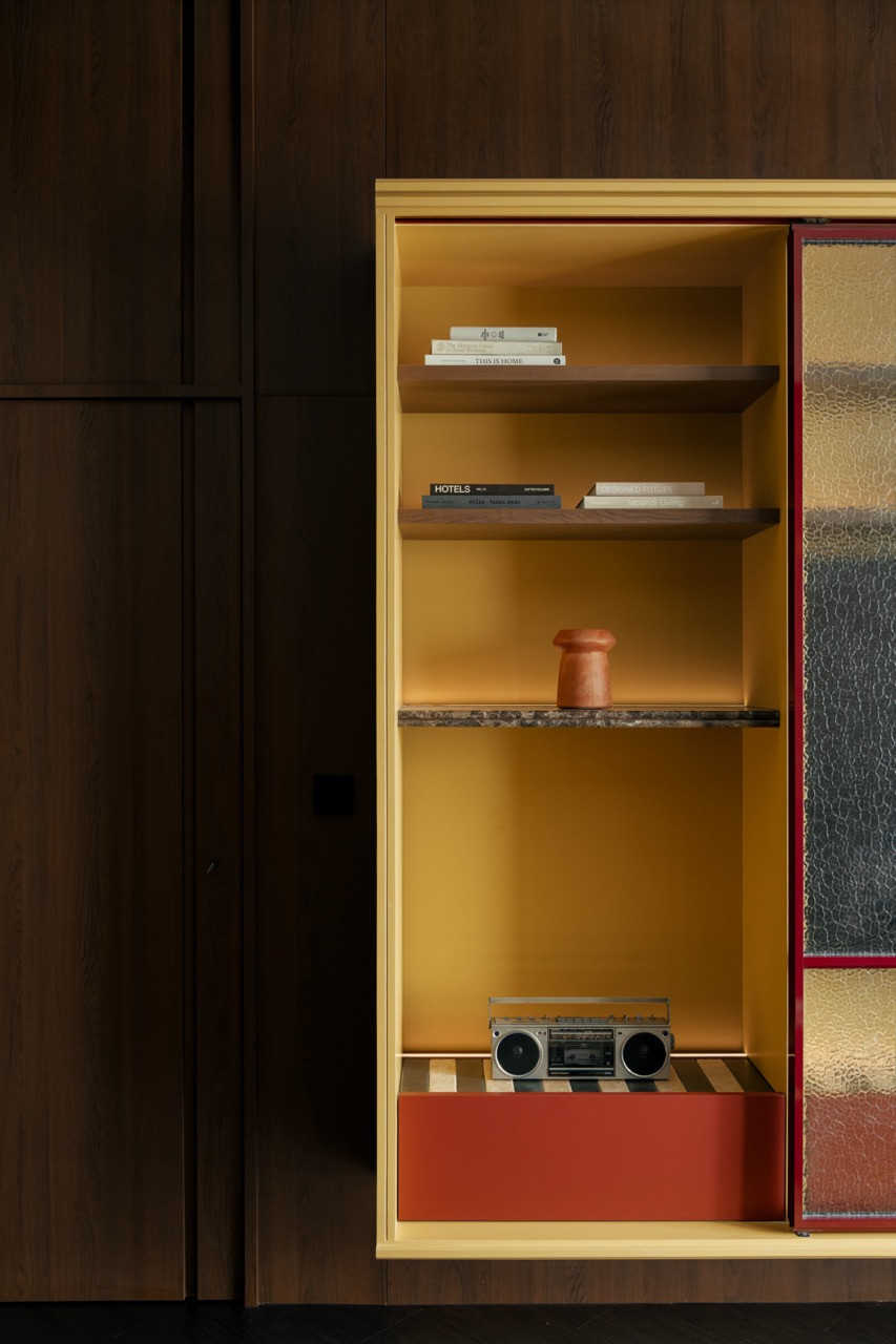 The mustard-yellow display cabinet opens to reveal walnut shelves holding design books, a terracotta vessel and a vintage boombox on the lower level