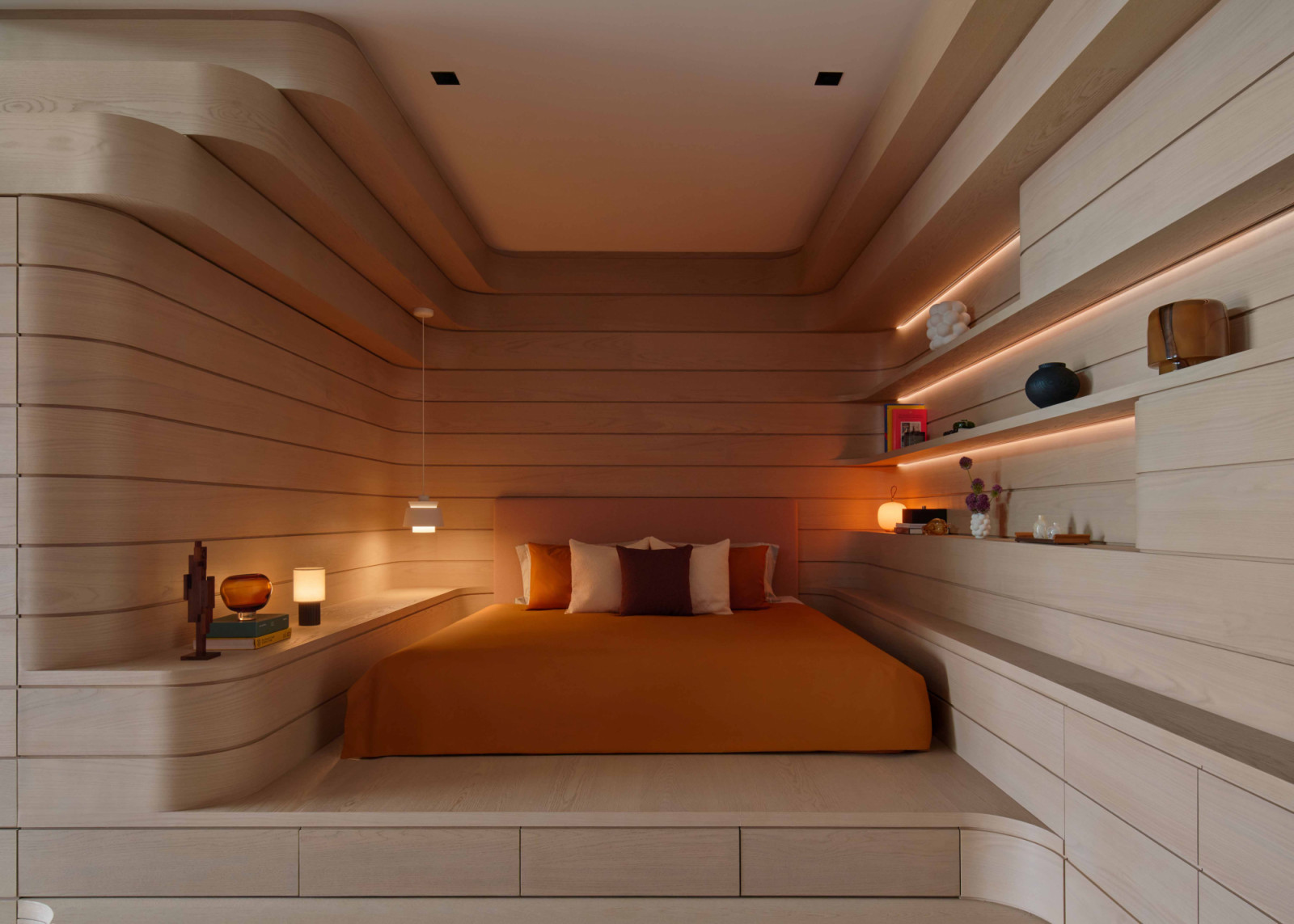 The bed is nestled within cove-like carpentry, with stepped drawers that double as storage and pull-out seats