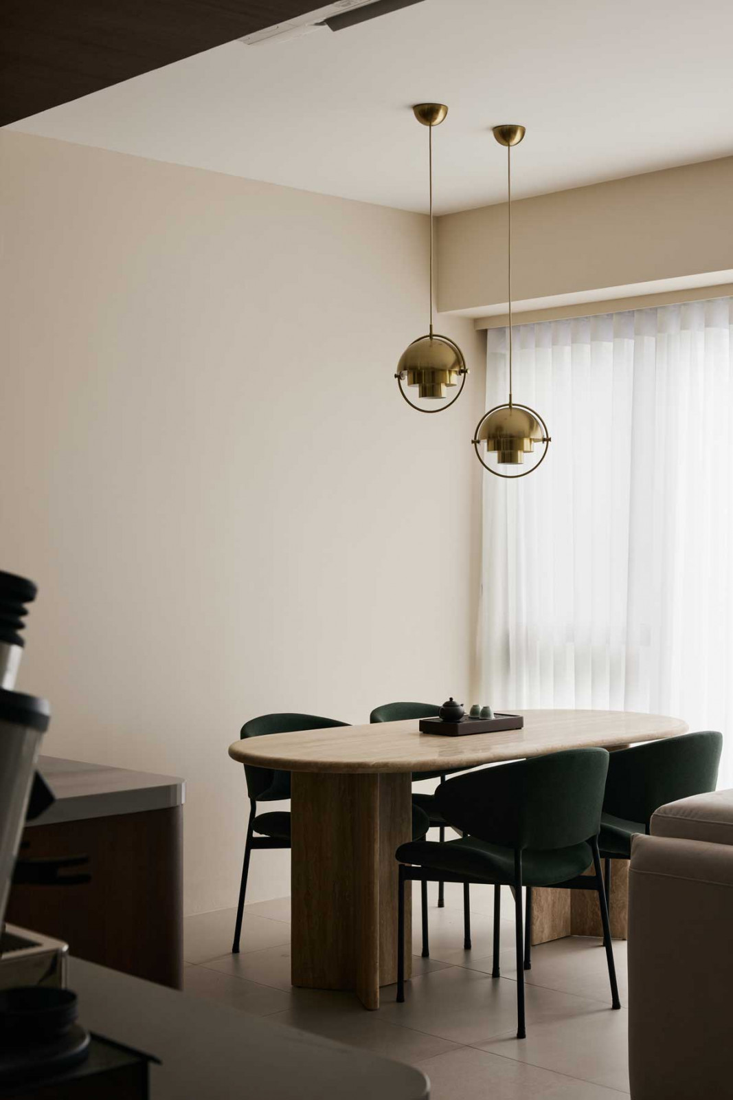 Twin pendant lamps float above a travertine dining table, their brass finish echoing the home’s warm, tactile palette
