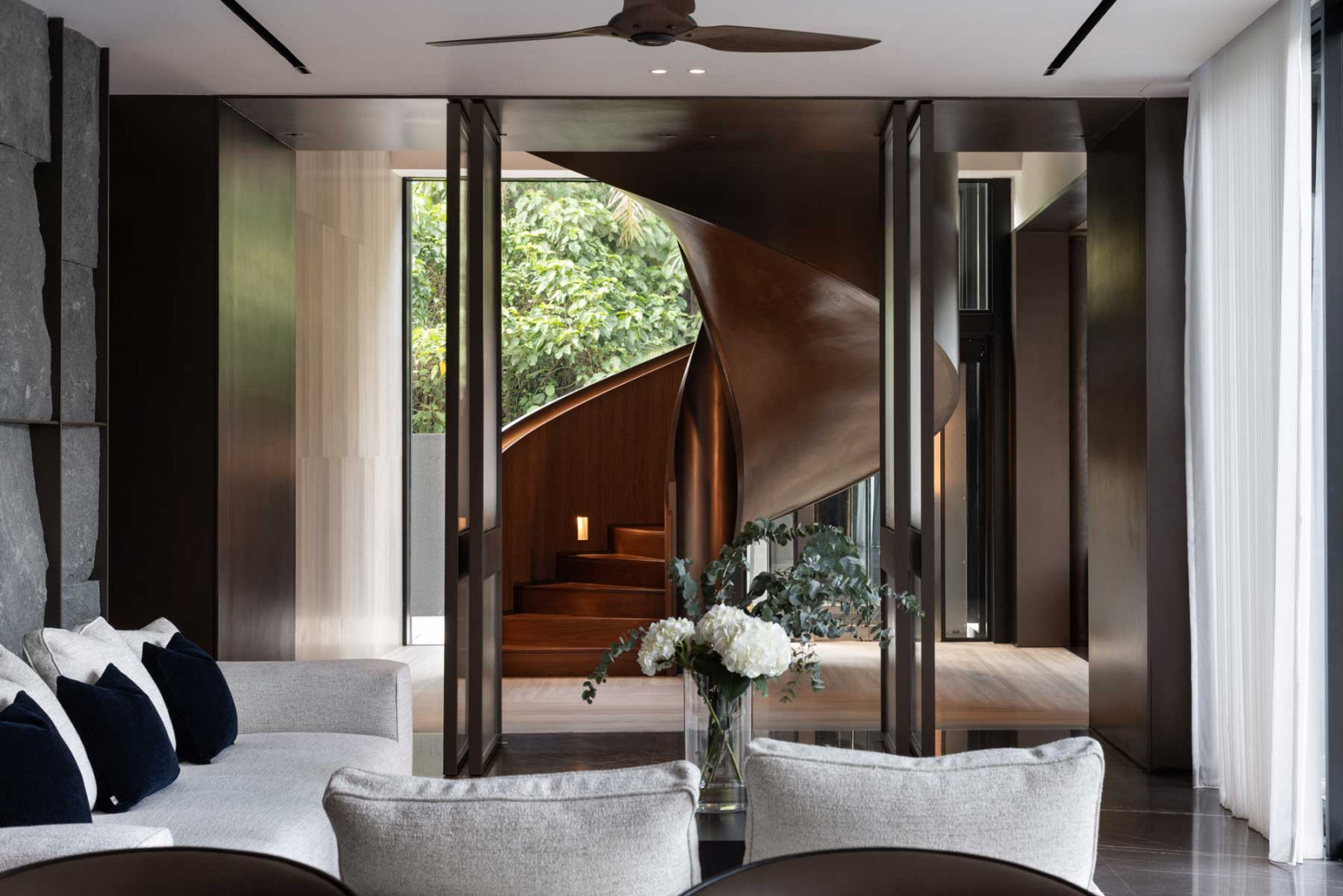 Pivoting panels allow the entertainment wing to be enclosed or opened up as needed, while a sculptural staircase acts as the architectural heart of the home