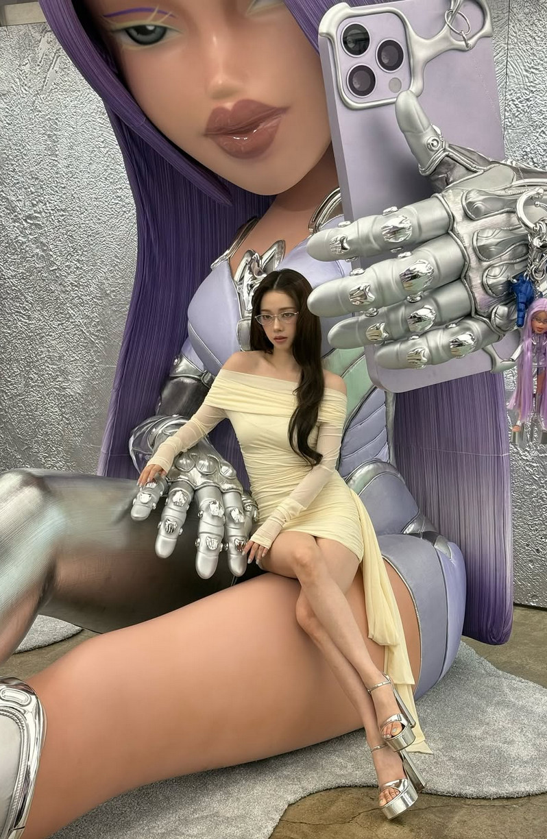 Karina in an asymmetrical cream dress perched within a giant metallic robot hand (Photo: @katarinabluu/Instagram)