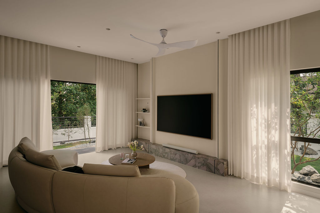 The living area, with a curved sofa from Ambient Living facing the TV wall, with the base of the TV cabinet clad in Palladium Sage quartzite