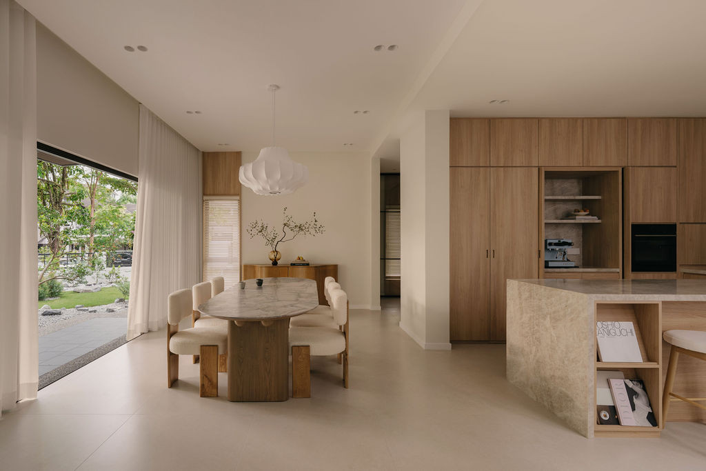 The dining and kitchen zone from the garden side, with the Nicchris dining table at the centre and the dry kitchen cabinetry in wood-textured laminate to the right