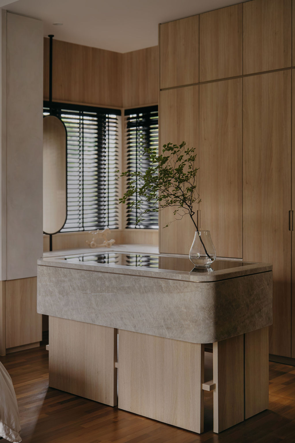 In the master bedroom, a stone-clad freestanding bathtub sits against floor-to-ceiling wood-textured laminate cabinetry
