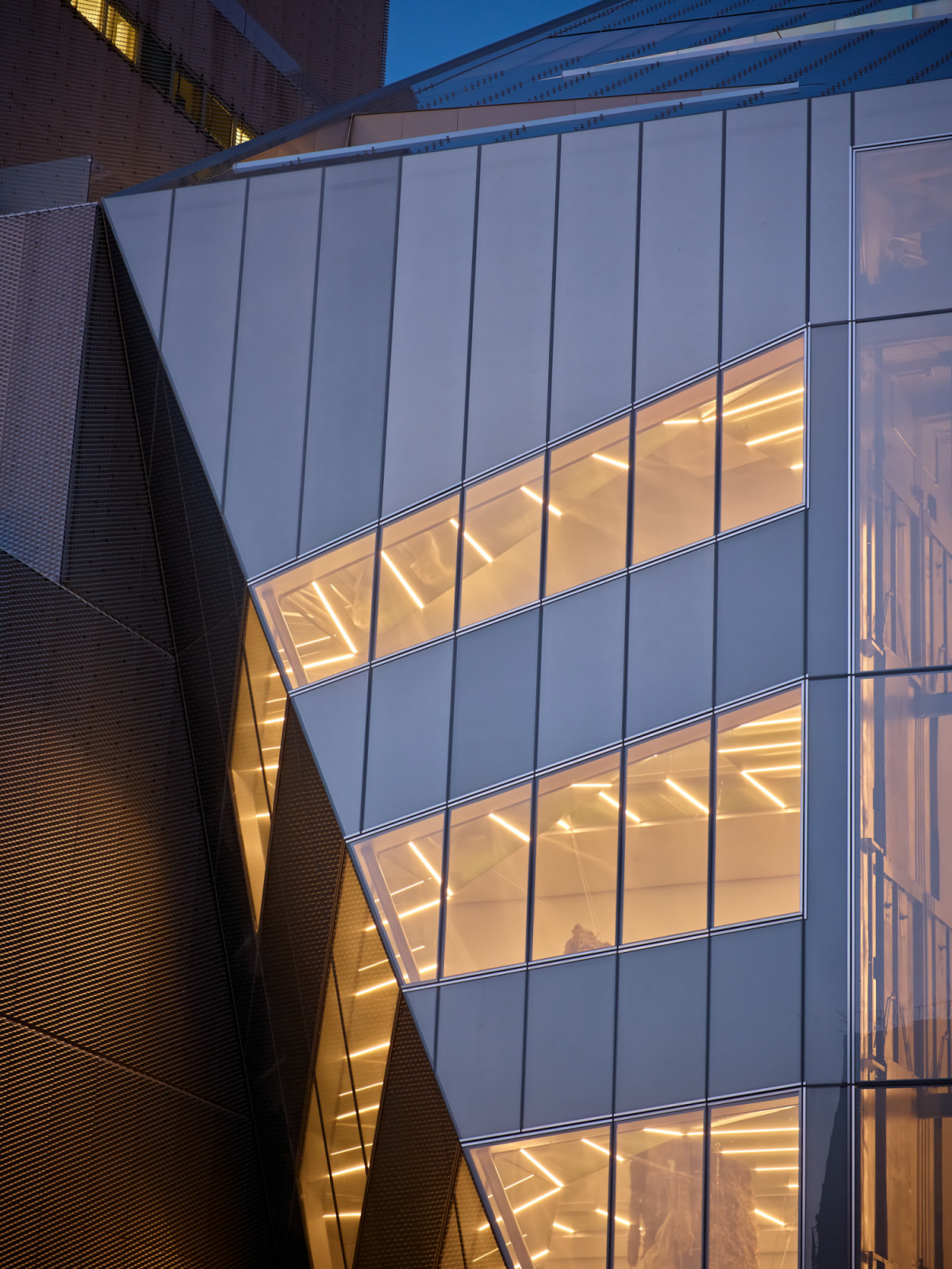 Detail of the OMA addition’s facade at dusk, showing the diagonal ribbon windows and the geometry of the laminated glass panels lit from within (Photo: New Museum)