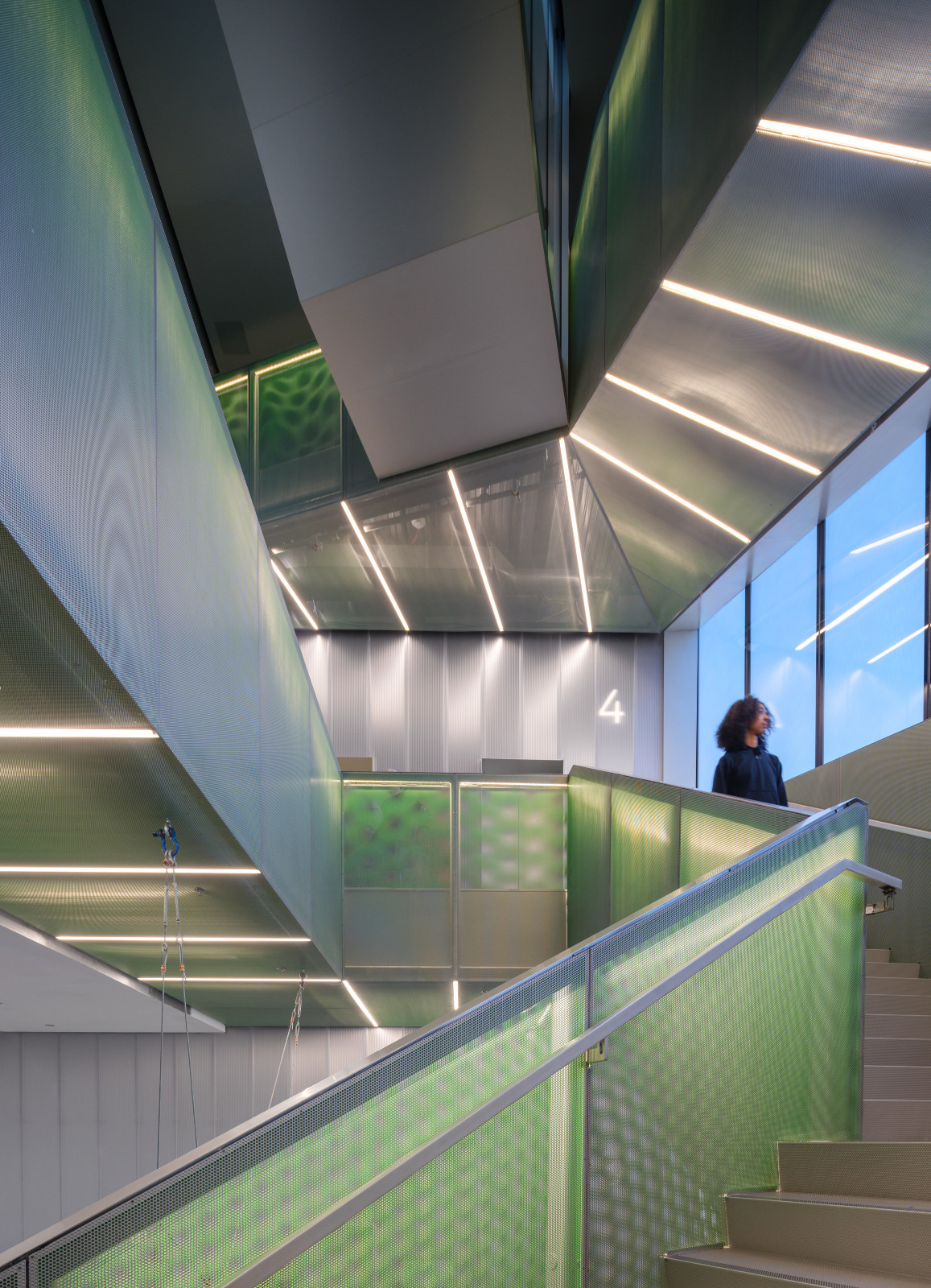 The atrium stair of the OMA addition, with green perforated panels, angled surfaces, and linear lighting visible across multiple floors (Photo: New Museum)