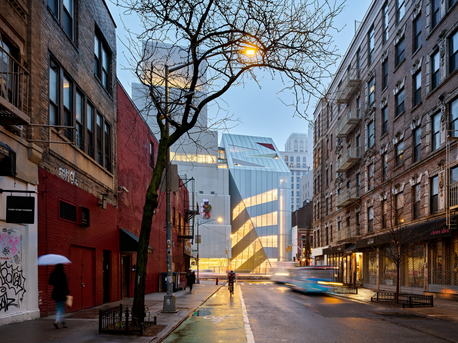 The OMA addition is seen from further along the Bowery, its laminated glass facade catching the last of the evening light against the Lower Manhattan skyline (Photo: New Museum)