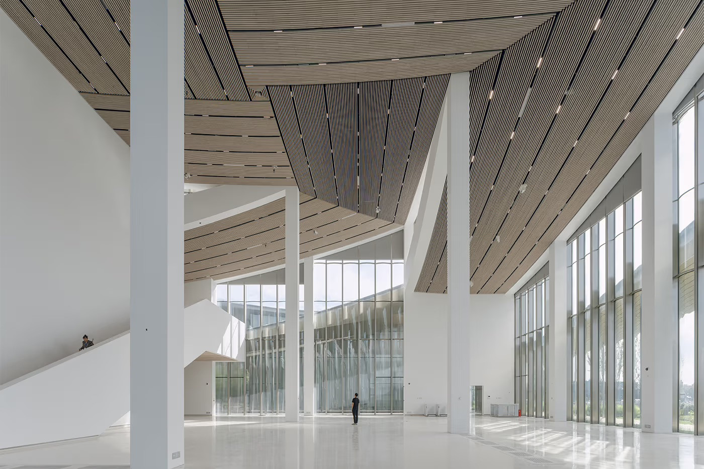 The main entrance hall of the Suzhou Museum of Contemporary Art is defined by a double-height interior, with its curving timber-batten ceiling and floor-to-ceiling glazing overlooking the courtyard gardens (Photo: BIG)