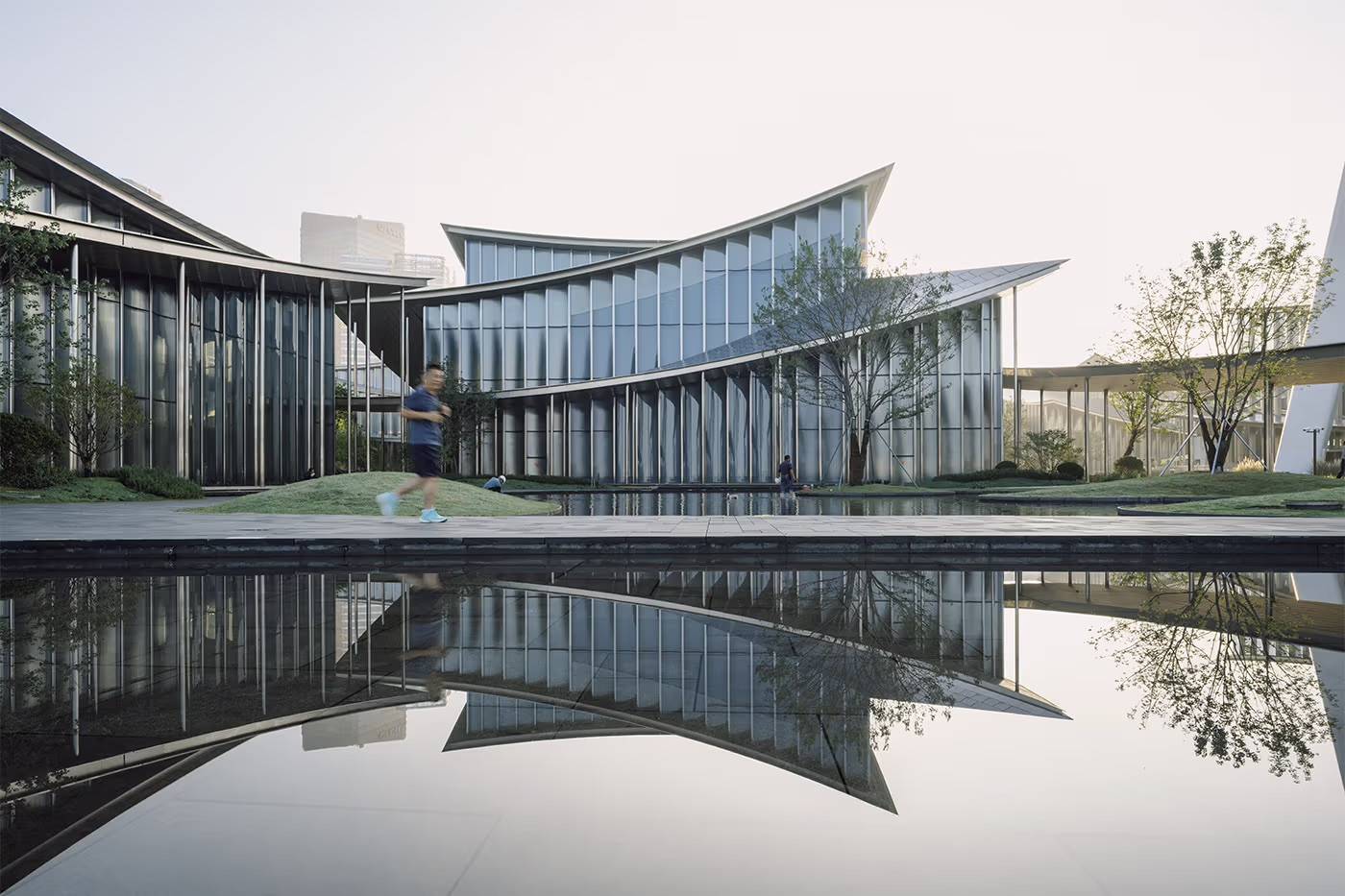 The ground-level courtyard of the Suzhou Museum of Contemporary Art, with the curved glass facades of two pavilions reflected in a still water feature (Photo: BIG)