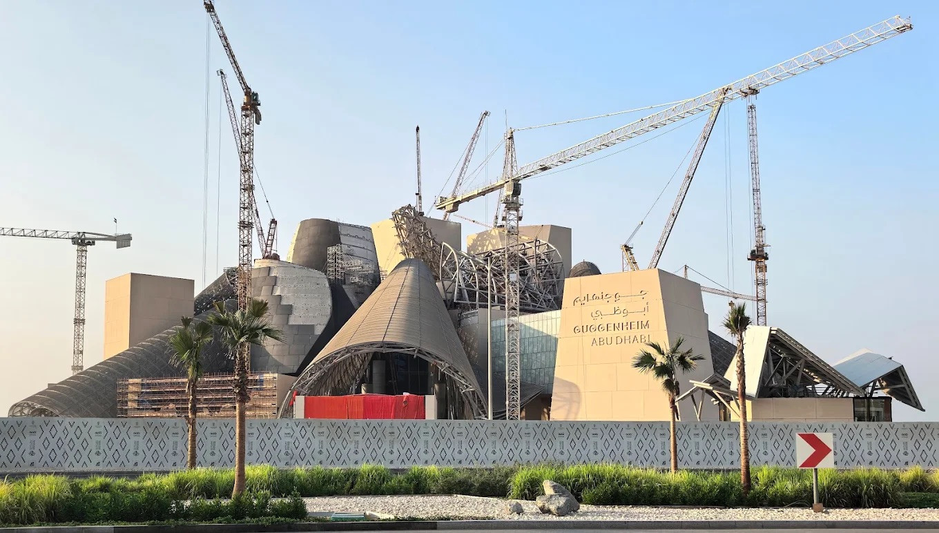 The construction site of the Guggenheim Abu Dhabi, showing the building’s distinctive cones and curved forms emerging behind the site hoarding on Saadiyat Island (Photo: Instagram/@f.y.i.arch)