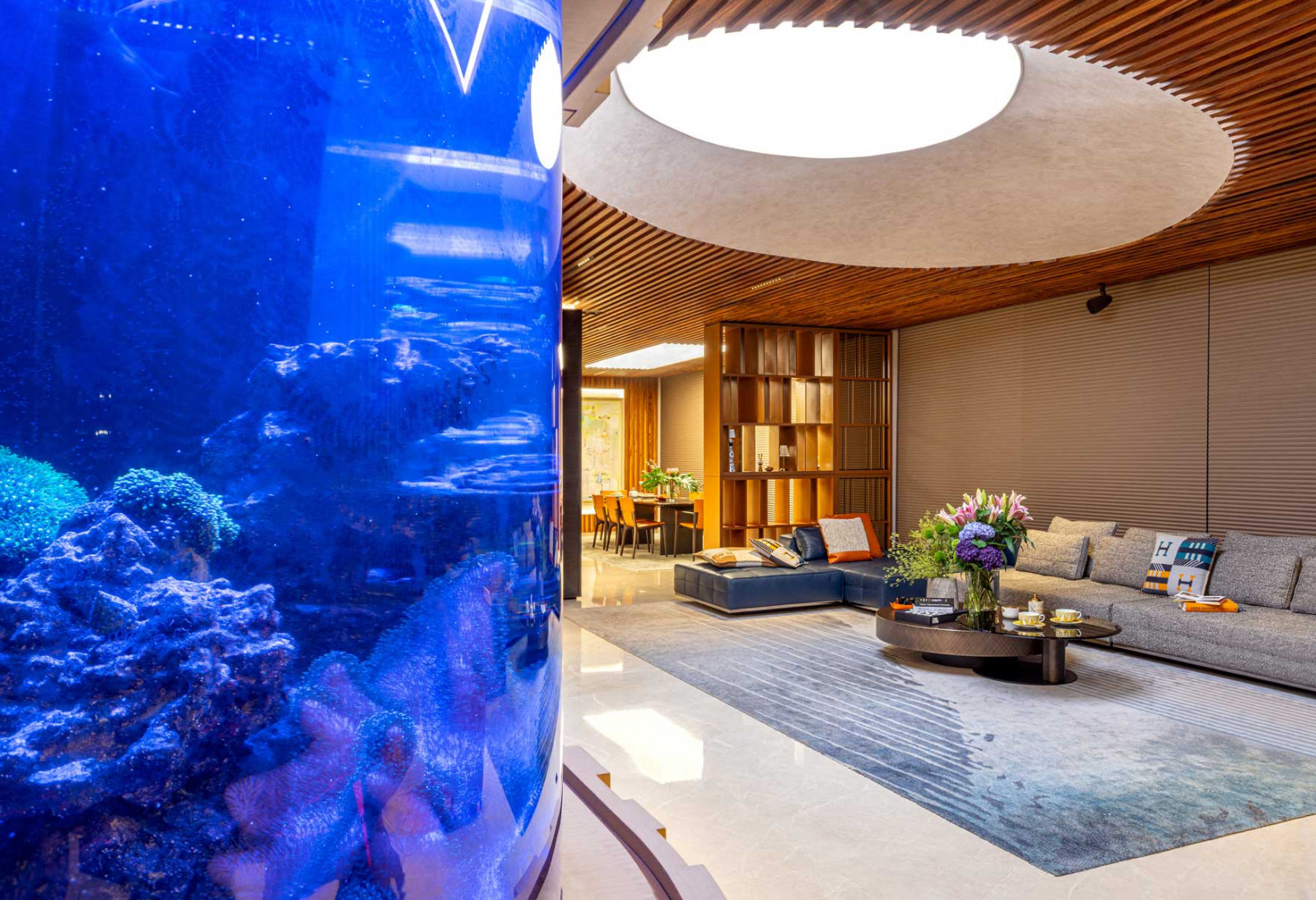At Soleil @ Sinaran, timber slats span the ceiling and walls to unify the dining and kitchen zones while the curved aquarium recalls the visual language of the interior
