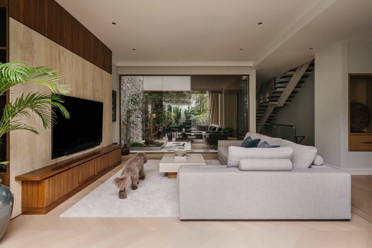 A wider view of the ground floor, showing the living room, the glass-enclosed courtyard beyond, and the staircase to the right