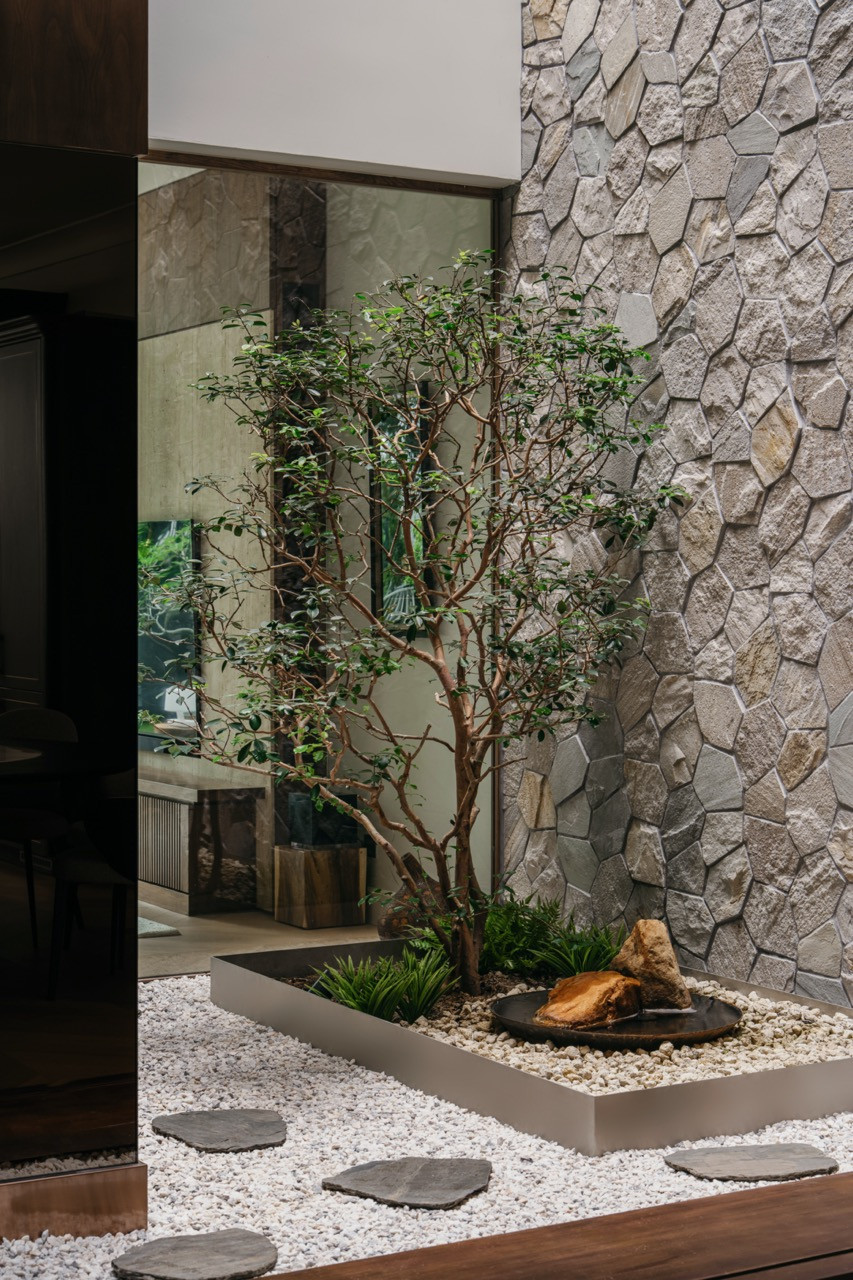 The sunken courtyard at ground level, with a tree planted in a gravel and stone bed, a water feature bowl, and the polygonal stone-clad wall rising behind