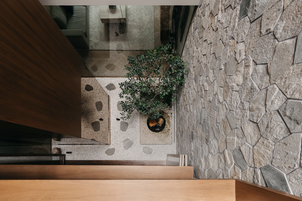 An aerial view of the courtyard from an upper level, showing gravel, stepping stones and the tree below, with the living area visible through the glass wall beyond