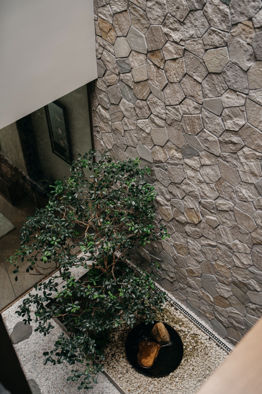 The sunken courtyard is seen from above, with a tree planted in a gravel bed and a water feature, set against the polygonal stone-clad wall