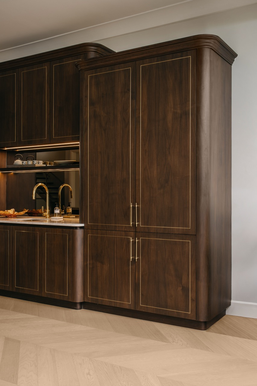 A full-height walnut pantry cabinet with brass inlay and brass handles, adjacent to the wet kitchen counter
