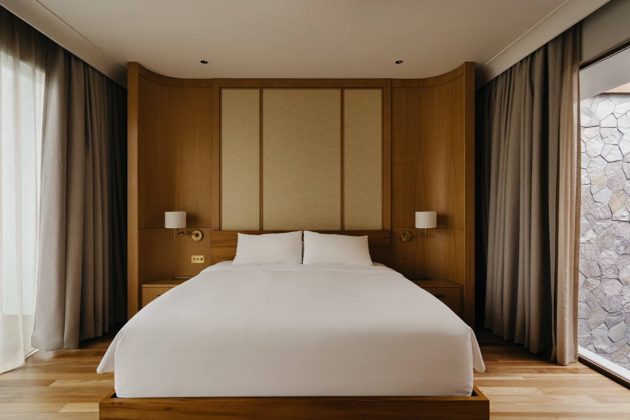 The master bedroom, with a woven wallpaper headboard panel recessed into a curved oak surround, flanked by brass swing-arm sconces
