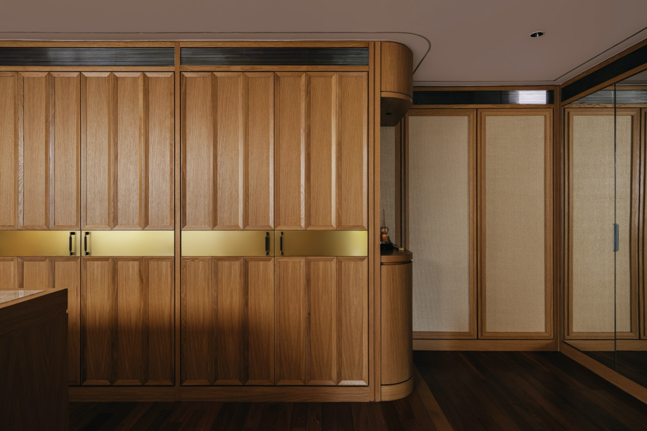 Oak wardrobe cabinetry with chamfered panel detailing, brass horizontal inlay bands and a curved corner