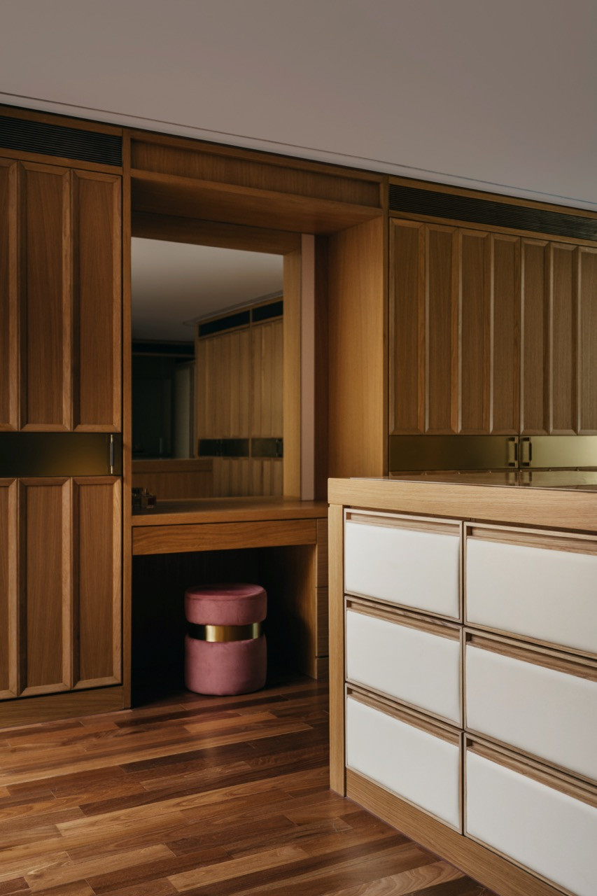 The master suite dressing room, with a built-in vanity nook, a pink velvet stool with brass base, and a white lacquered drawer island set within walnut joinery