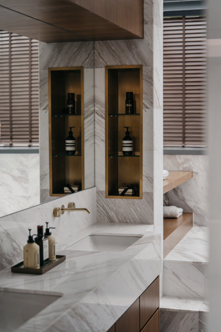 The master bathroom, clad in marble with brass-framed recessed niches and a wall-mounted brass tap