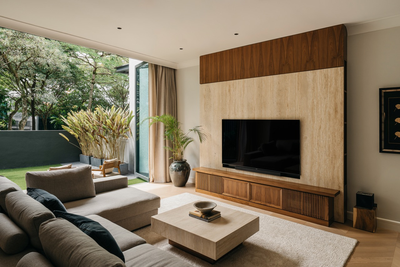 The living room, with the travertine and walnut TV wall, a slatted timber media unit, and full-height glazing opening onto the entrance garden beyond