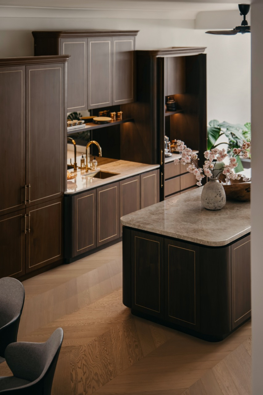 The wet kitchen seen from the dining area, with dark walnut cabinetry, brass inlay, a mirrored splashback and the marble-topped island