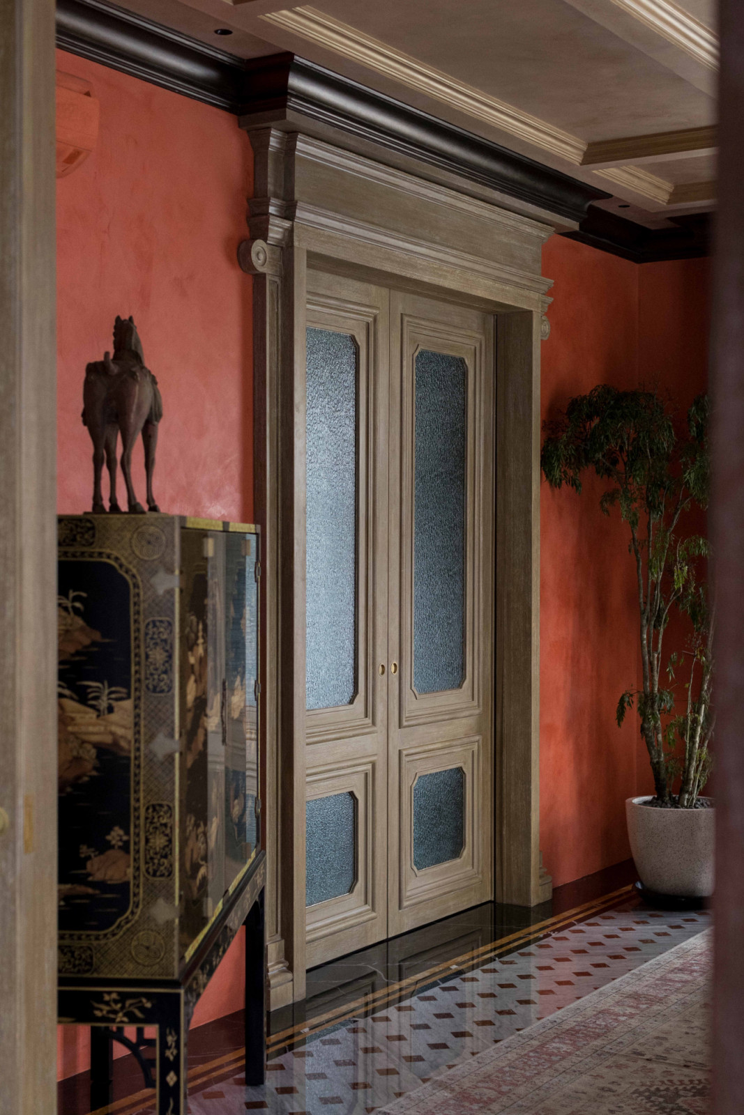 Parisian-style boiserie frames a pair of double doors set against the home’s signature orange walls