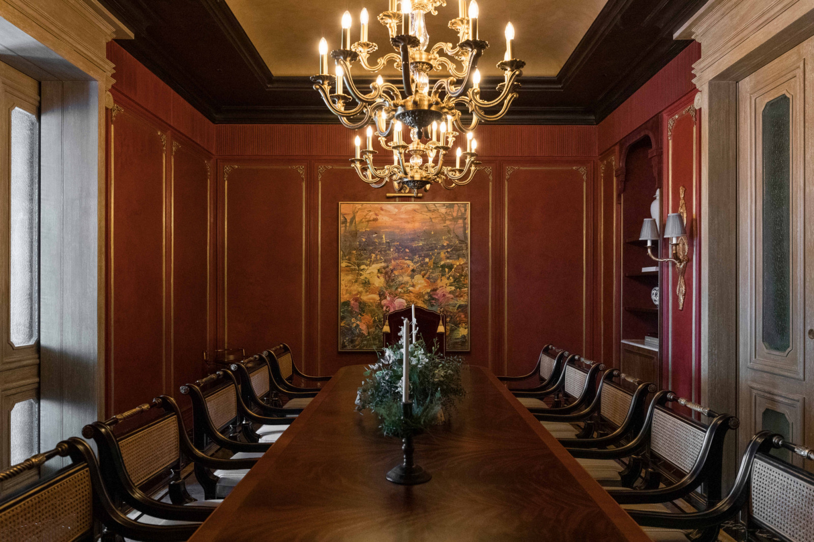 An elongated dining table is paired with chandeliers, russet walls and classical panelling
