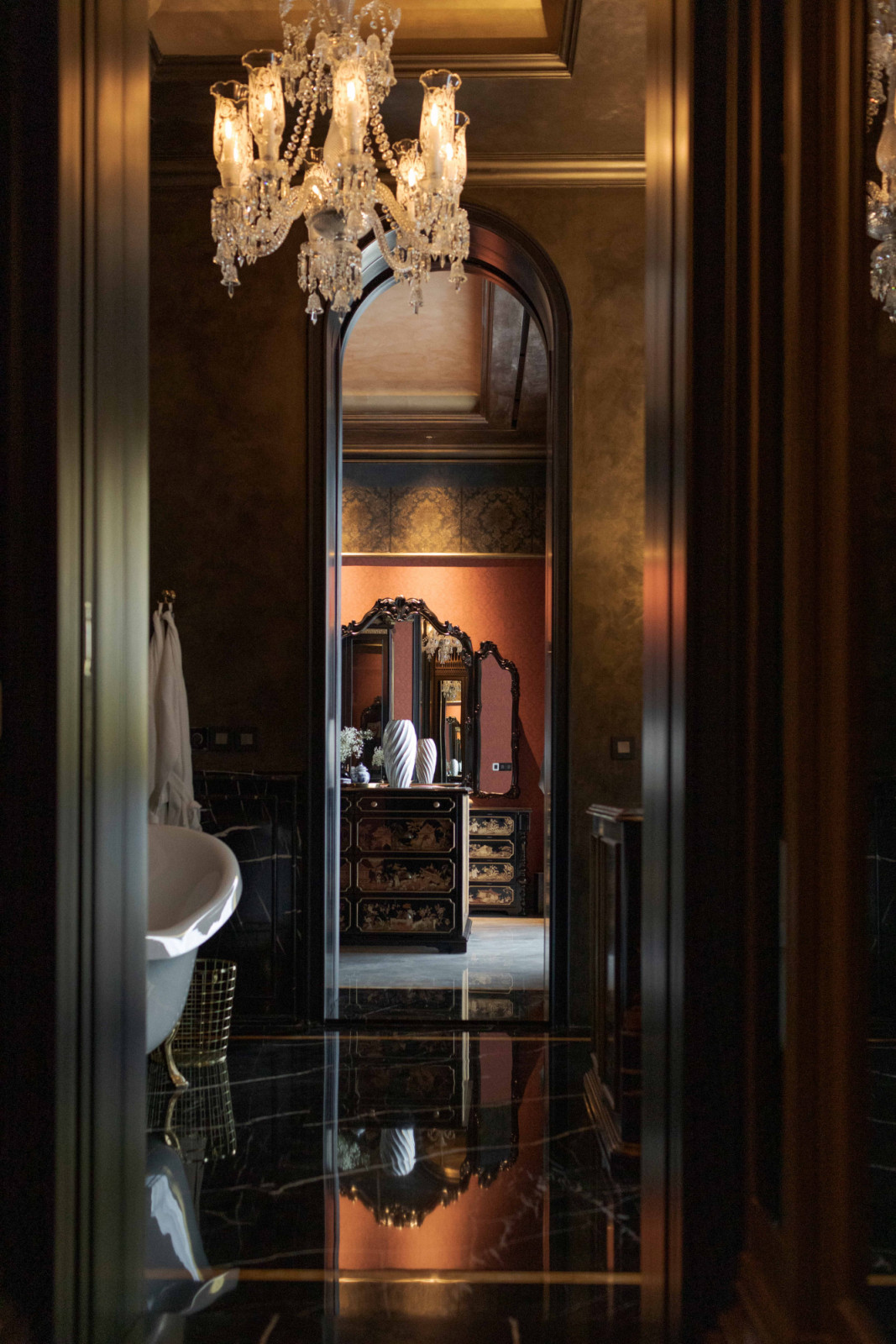 A layered view of the bathroom and vanity at The Continental, articulated with a chandelier, terracotta finishes and a clawfoot bathtub