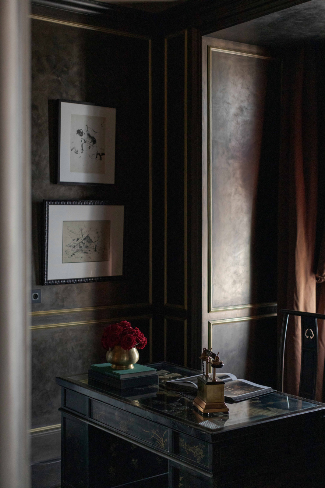 A writing desk stands against richly textured walls trimmed with gilded mouldings