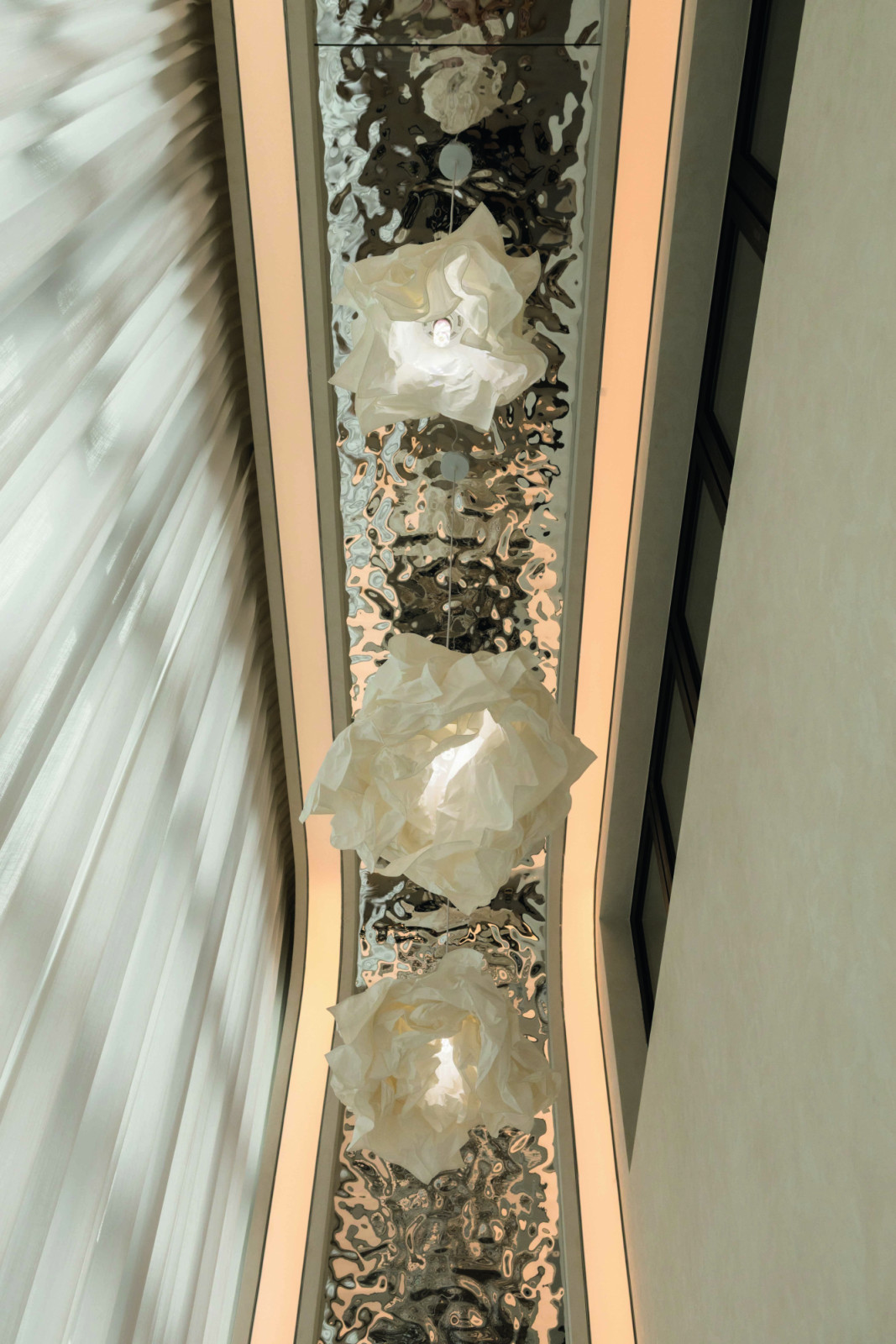 Metallic finishes catch the shifting natural light, animating the ceiling plane that is adorned with pendants