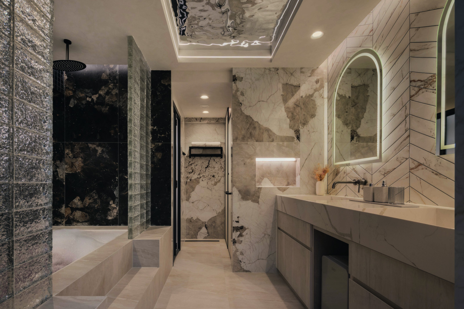 The ensuite pairs veined stone surfaces with softly lit mirrors and layered lighting for a refined, hotel-like atmosphere