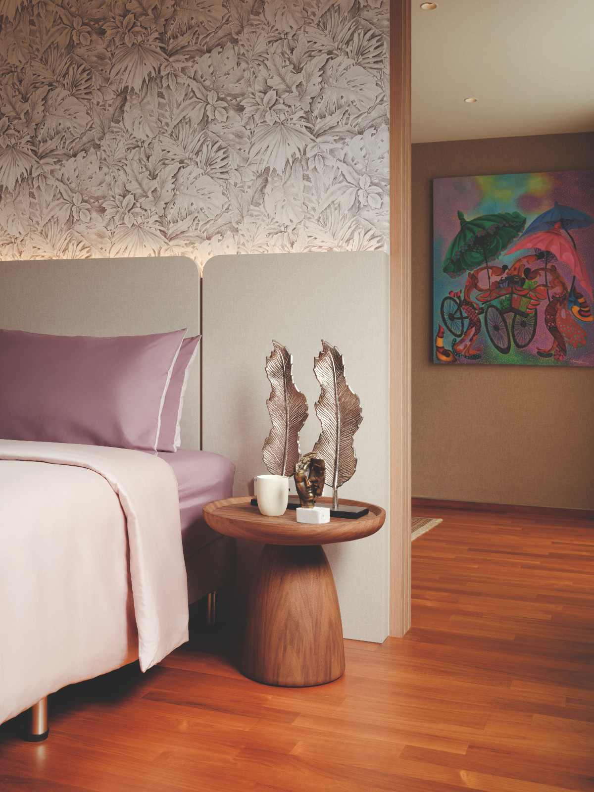 A monochromatic tropical-themed wallpaper adds texture above the bed, contrasted by a vivid artwork set just beyond