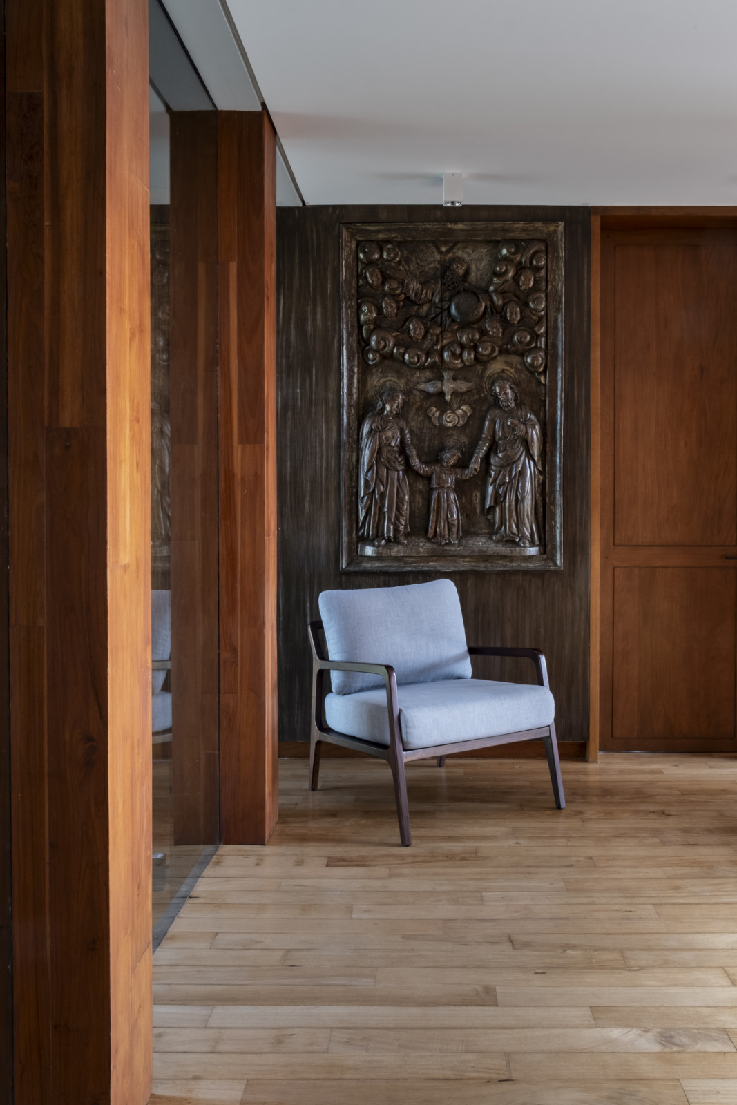 A blue midcentury-style chair is placed beneath a handcarved religious wooden relief in a Batangas, Philippines home designed by LYS Architecture
