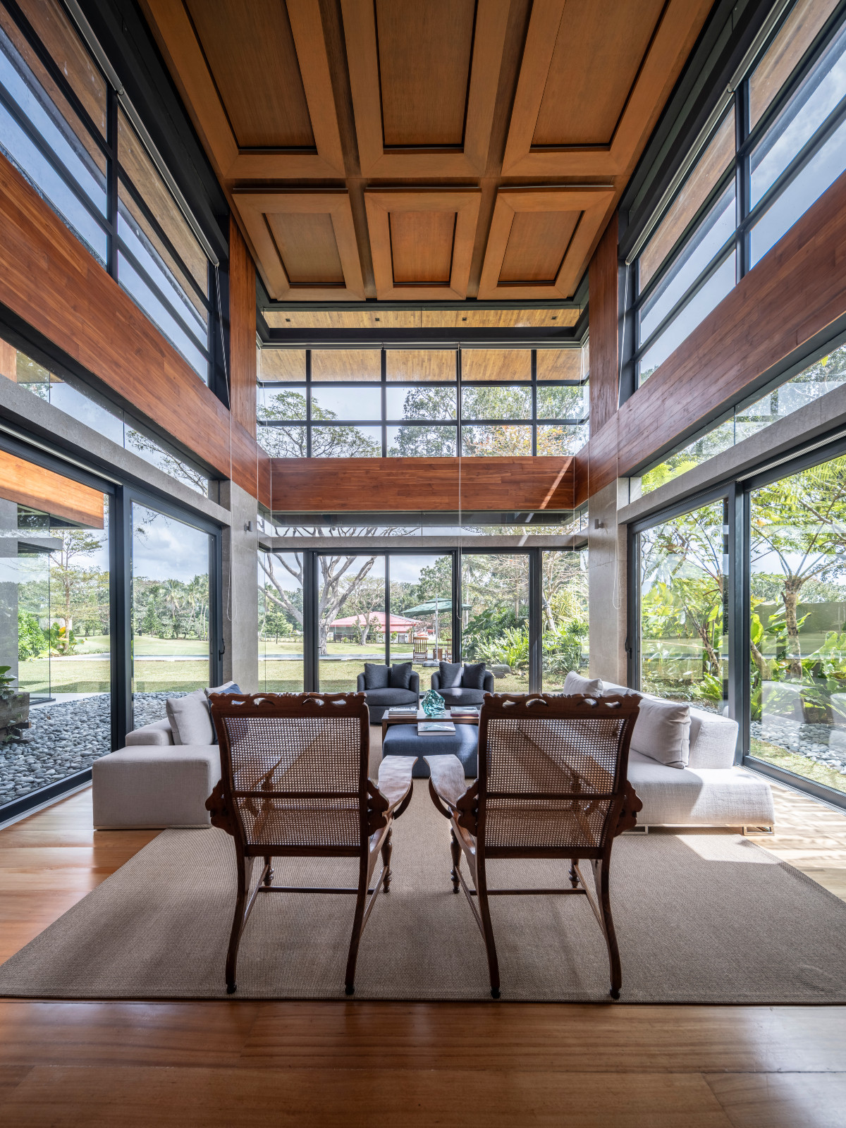 The sitting room is a melange of beiges and blues, modern linen upholstered sofas juxtaposed with antique caned colonial-style chairs in a Batangas, Philippines home designed by LYS Architecture