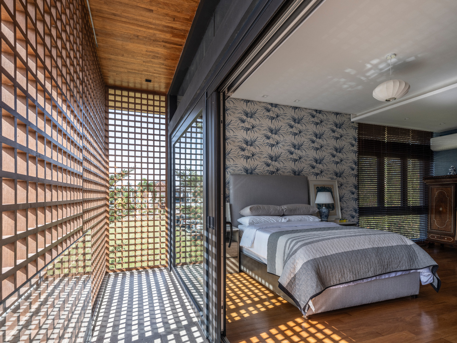 The bedrooms in a Batangas, Philippines home designed by LYS Architecture all adapt to nature, and the screens provide ventilation; this one is no exception, as its blue wallpaper and bed reflect the home’s overall calm atmosphere
