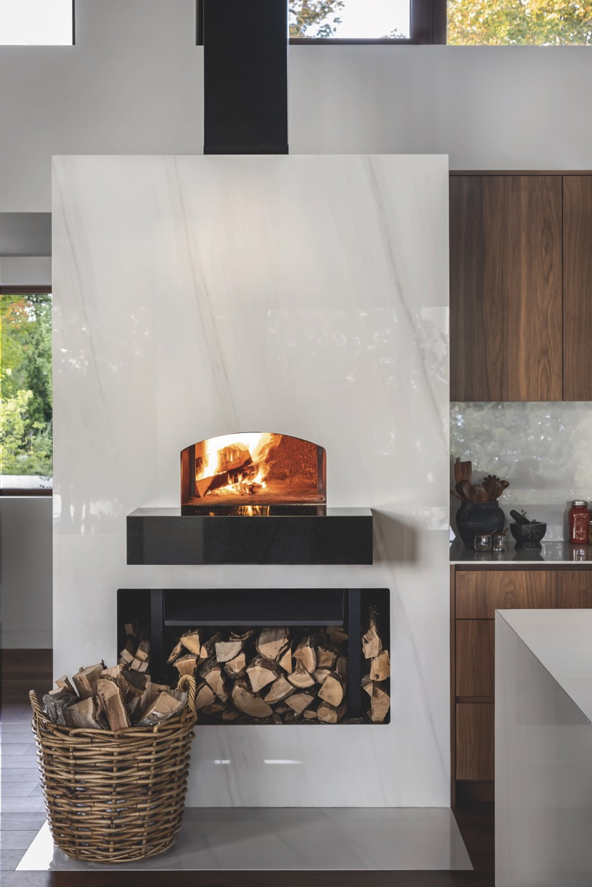 The pizza oven itself, clad in countertop porcelain, features a thermally sealed door and replaces the traditional fireplace