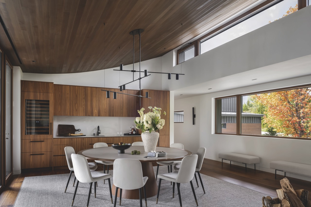 The custom pendant lighting above the dining table integrates with the curved cedar ceiling