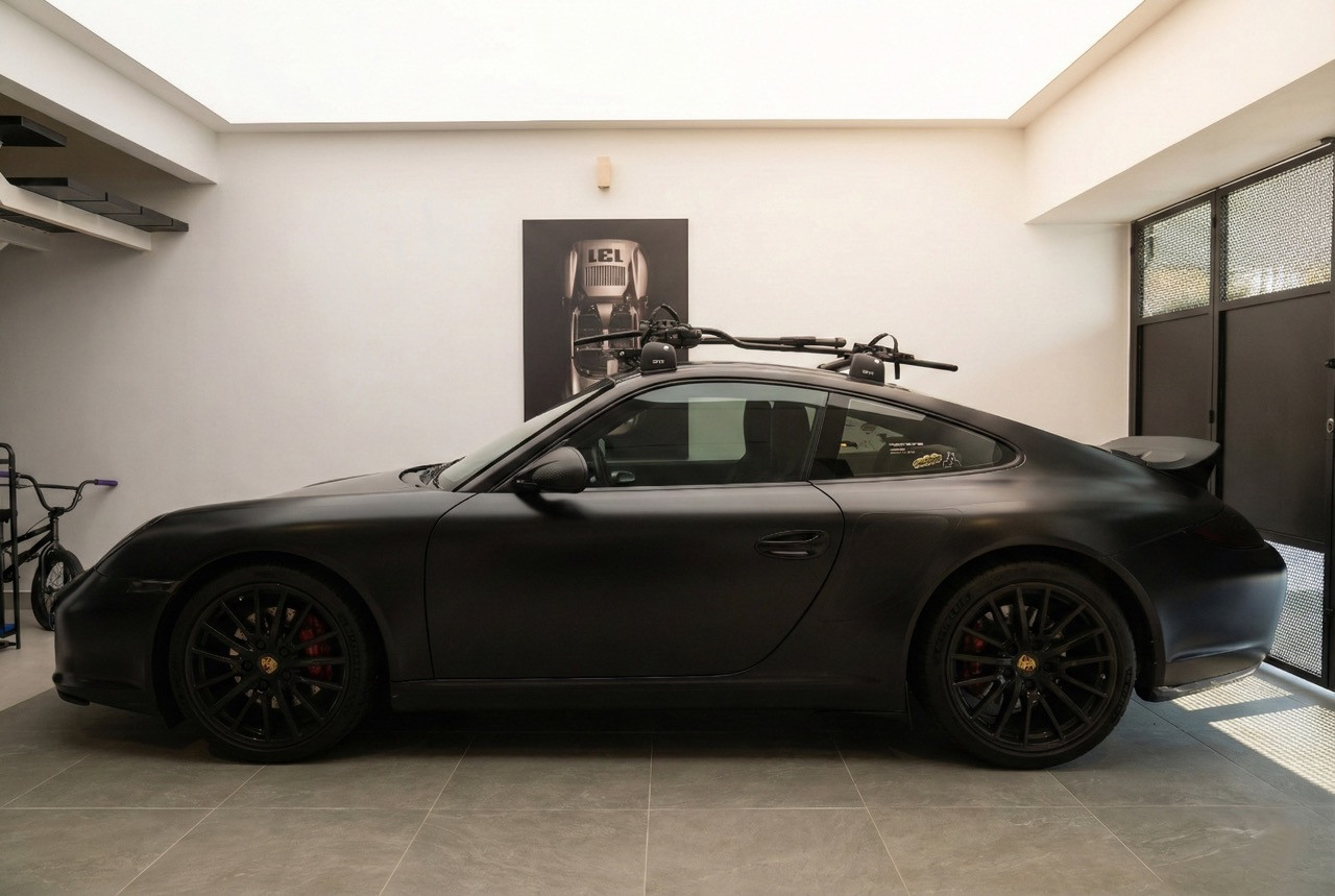 A matte black Porsche 911 parked inside the ground-floor garage beneath a membrane ceiling