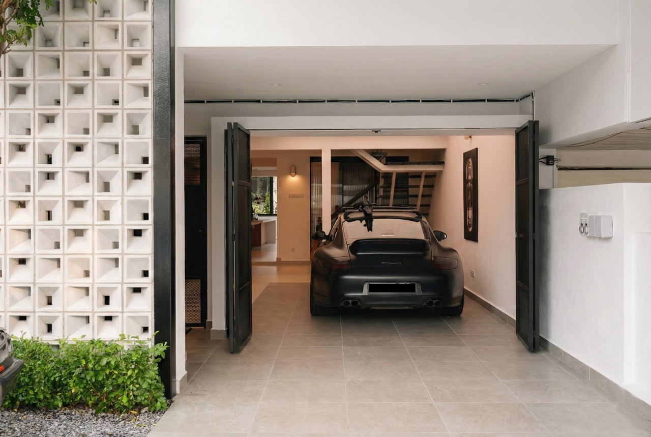 The perforated steel folding garage doors open to reveal a matte black Porsche 911 parked inside, with the concrete screen wall to the left and the living interior visible beyond