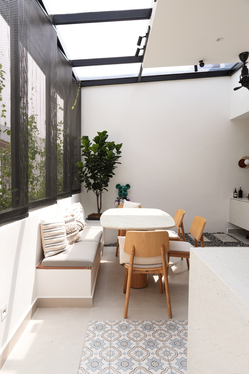 The rear dining area under a glass roof with built-in banquette seating, a marble-topped table, timber chairs, and perforated steel screening with climbing plants; encaustic patterned tiles in the foreground