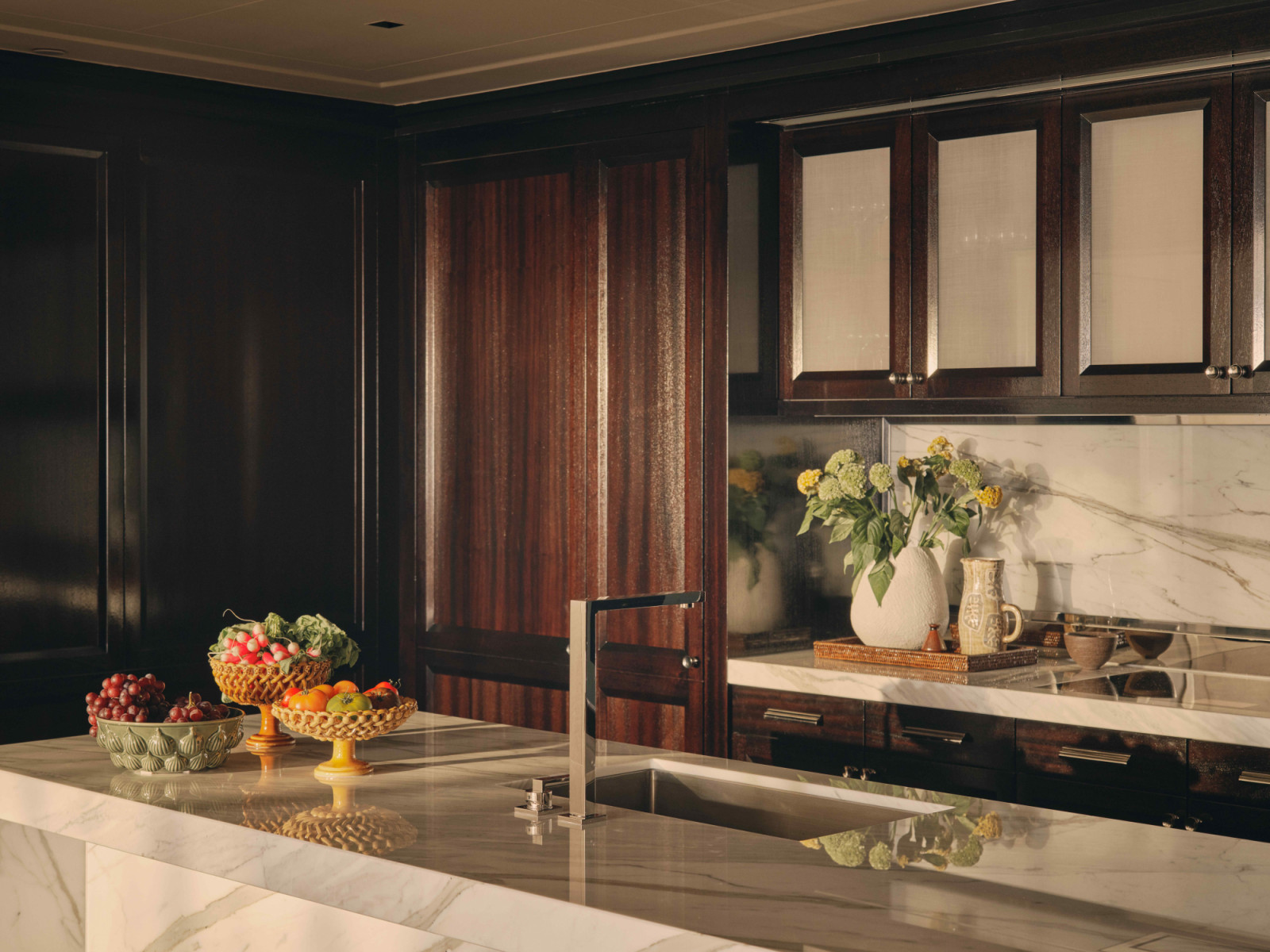 The kitchen features cabinetry of rich timber make, layered and softened with marble tops
