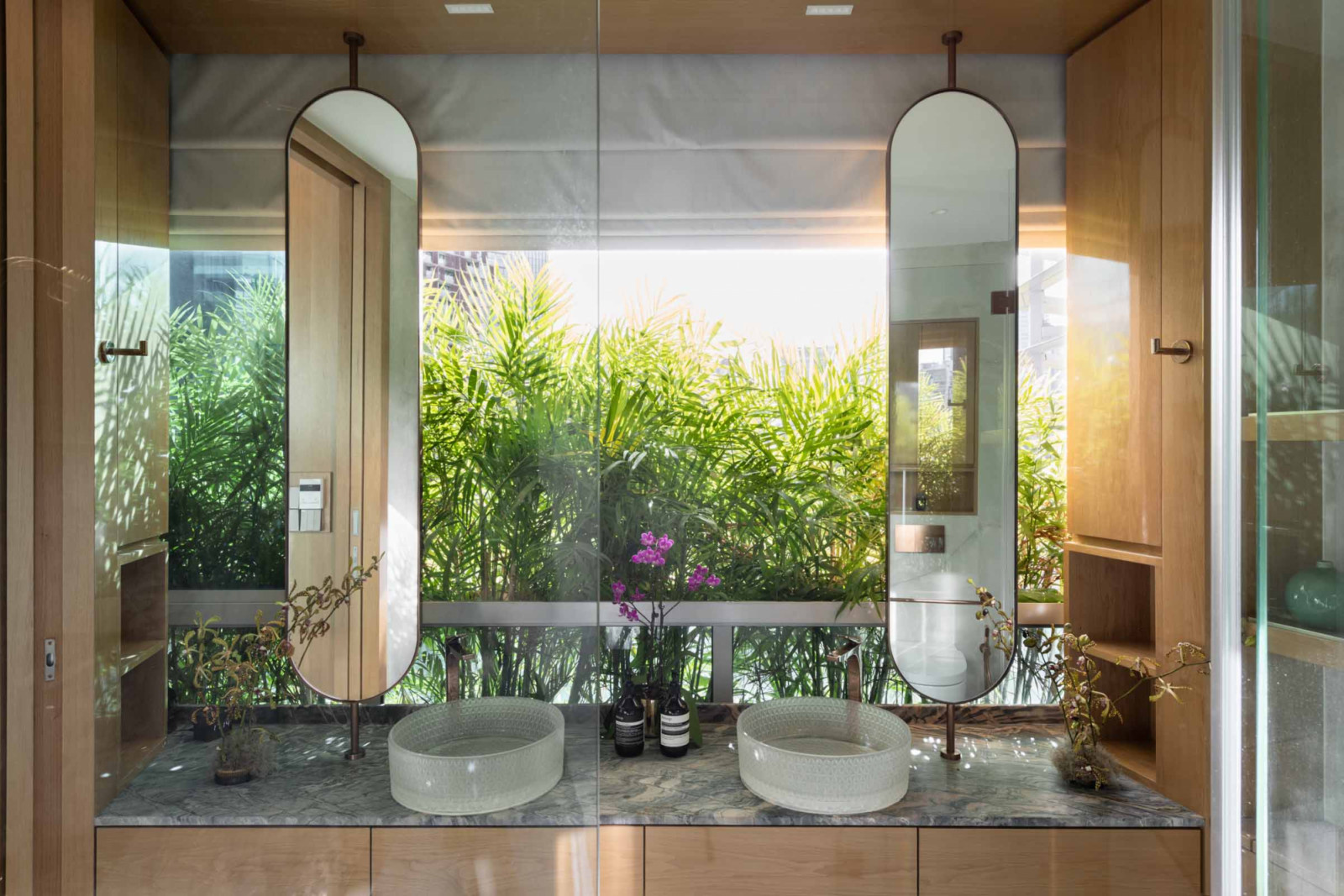 The master bathroom feels like a tropical resort with the verdant greenery in the background, while the frosted basins lend a playful, bespoke touch