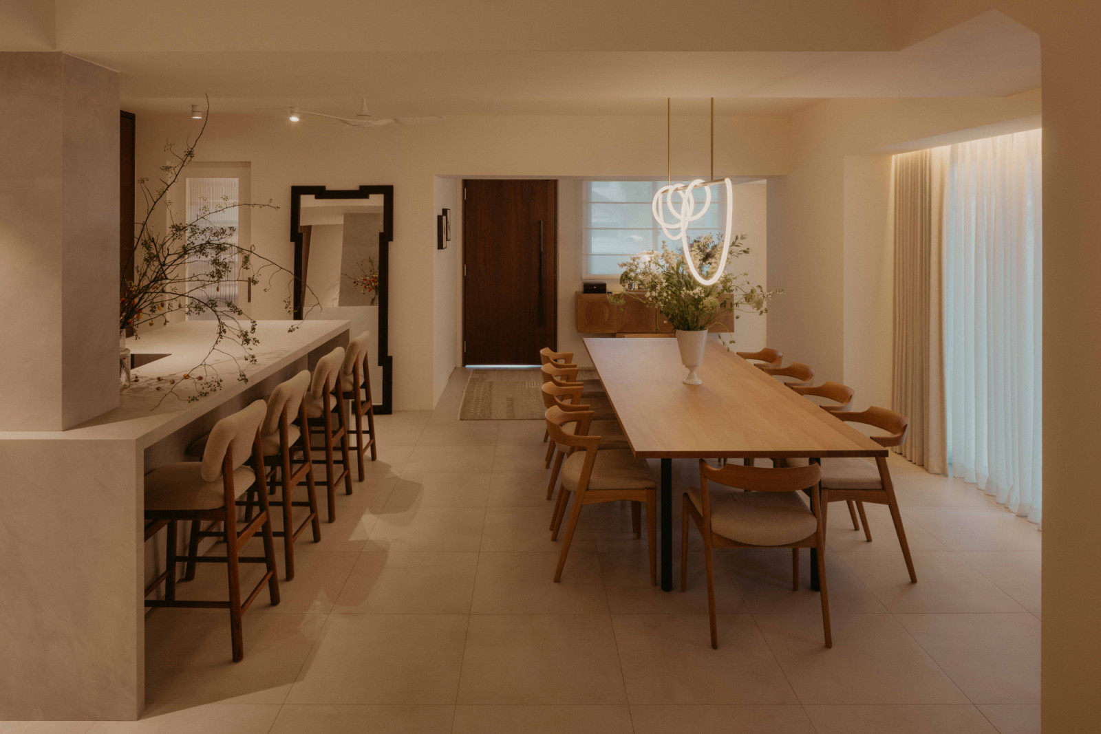 The dining area is anchored by a long timber table and sculptural pendant, with the kitchen island positioned alongside to encourage gathering