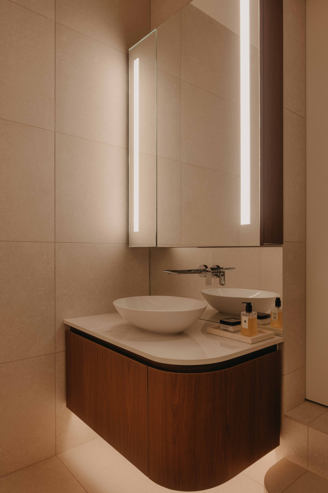 A floating vanity in warm timber is paired with a vessel basin and softly lit mirror in this West Coast home, with a top in Dekton Helena by Cosentino